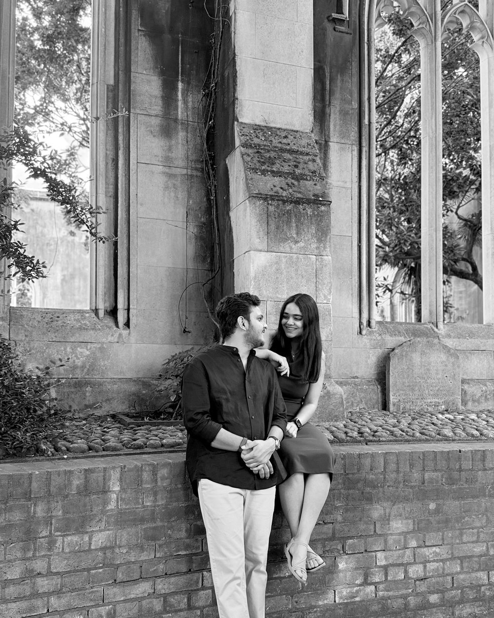 Raj and Lavina sitting on a brick wall beneath stone arches